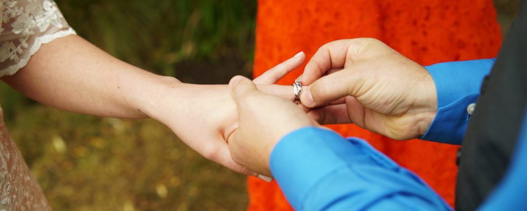 person placing a wedding band on another person's hand