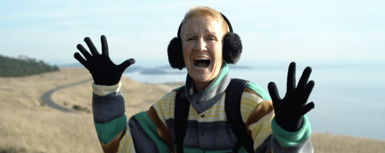 excited woman wearing black gloves and ear muffs with the sea in the background
