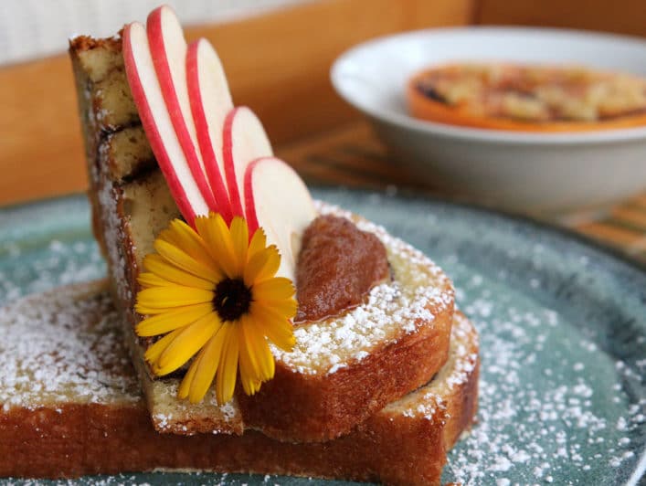 Plate of french toast topped with a fan of sliced apples and a flower garnish