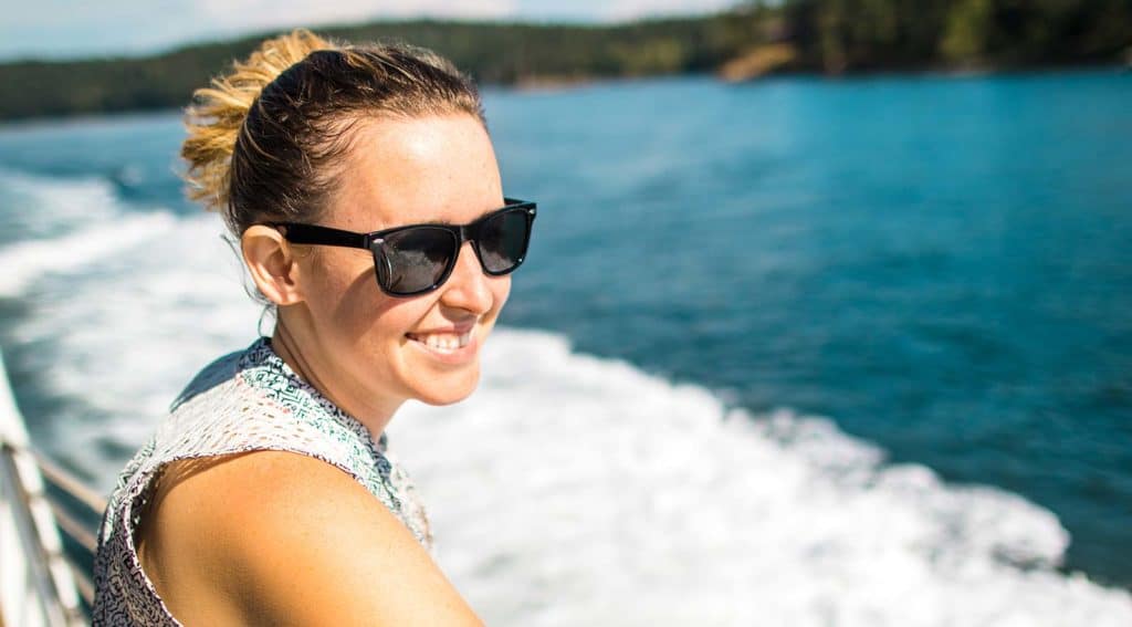 Woman wearing sunglasses smiling while looking out across the water