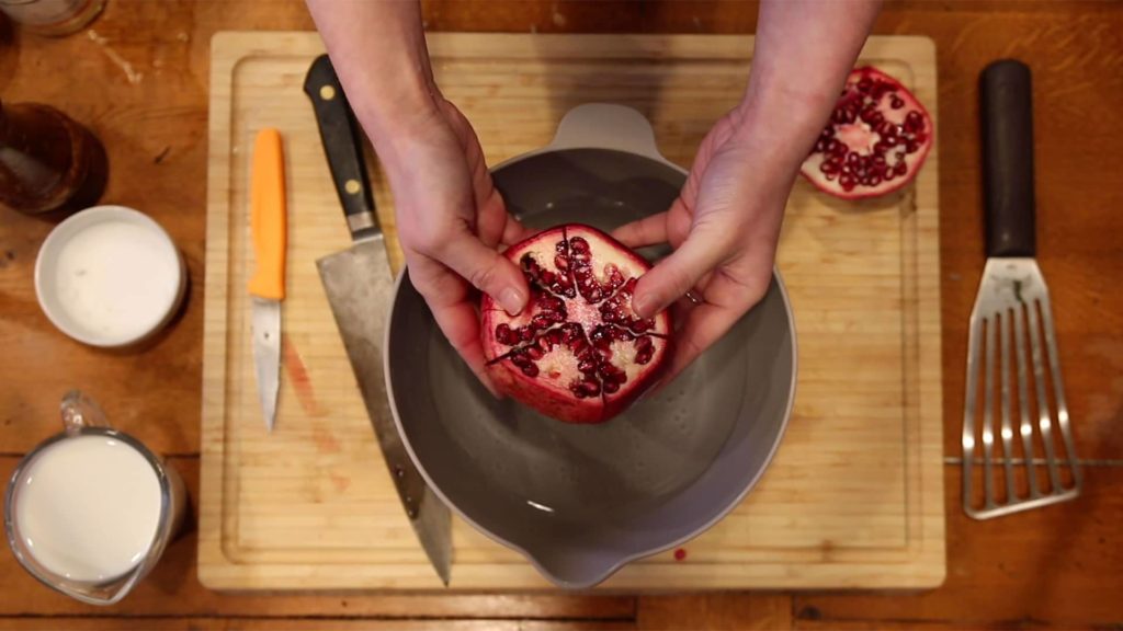 hands holing a pomegranate with the top cut off