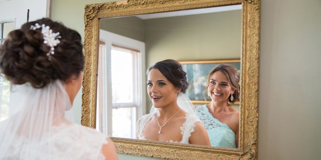 Bride and attendant looking at her reflection in a mirror
