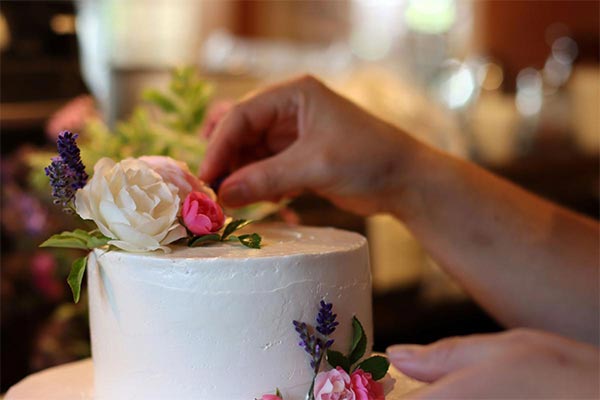 cake being decorated with small white, pink and purple flowers