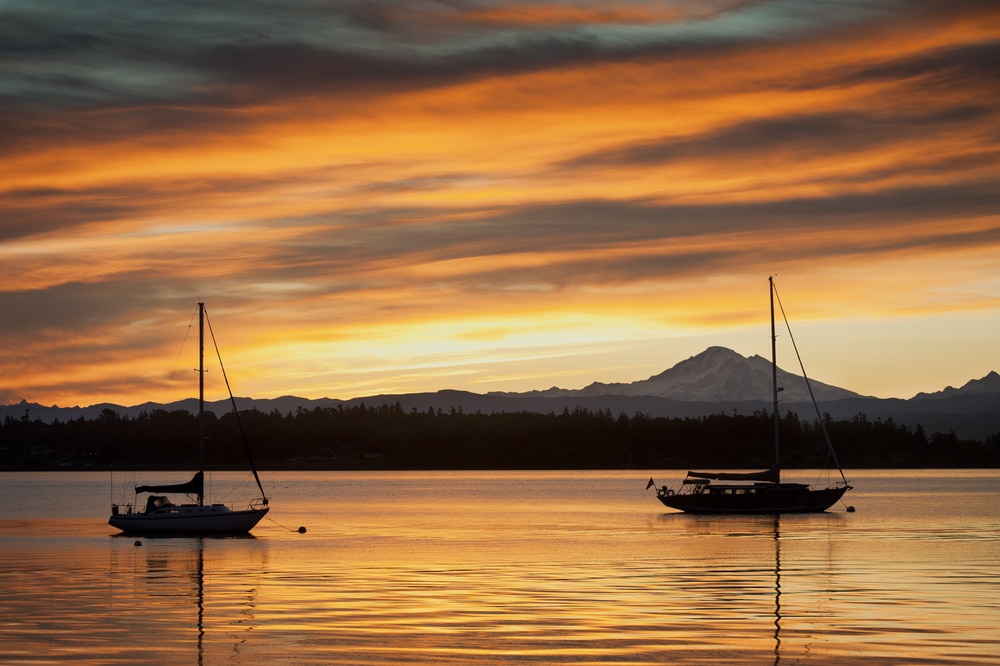 Two sailboats moored in still waters at sunset with mountain in the background