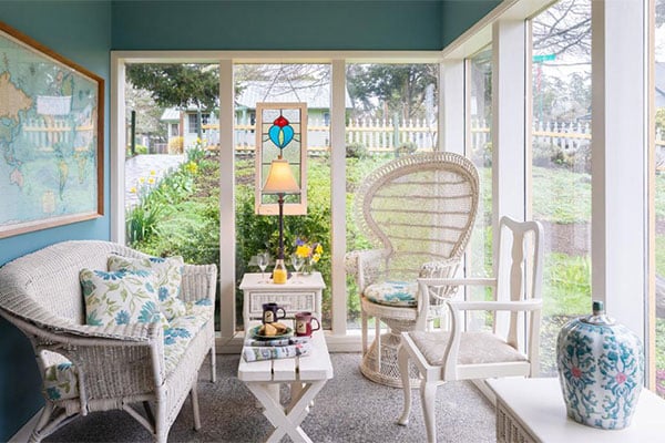 sunroom with white wicker furniture and coffee mugvs and scones set on the table